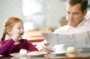 Father reading paper at cafe with his little daughter